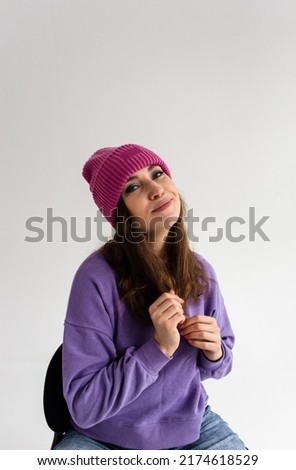 Beautiful young woman in purple hat and sweatshirt on gray background in studio
