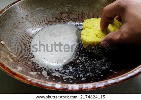 Selective focus of human hand scrubbing or cleaning a burnt, scorched and greasy pan or wok on kitchen sink. Royalty-Free Stock Photo #2174624115