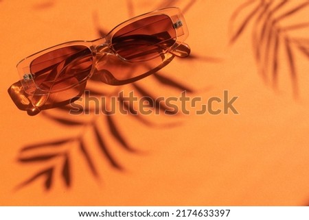 Orange sunglasses on an orange background with shadow from a palm tree. Summer background. Vacation. Place for text. Selective focus.