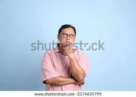 The adult Asian man with pink shirt standing on the blue background.