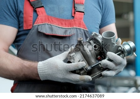 Car maintenance. An auto mechanic holds a new turbocharger in his hands. Inspection and control of the spare part for the engine for compliance and integrity. Royalty-Free Stock Photo #2174637089