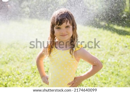 Happy child girl playing with garden hose and having fun with spray of water in sunny backyard. Summer time. Kid Boy helps water garden with hose. Slow life. Enjoying the little things. Summer holiday