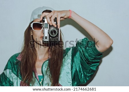 Cool teenager. Fashionable girl in colorful trendy jacket and vintage retro sunglasses with camera film in 80s - 90s style. Teenage girl at the disco, on a white background. Royalty-Free Stock Photo #2174662681