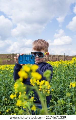 The boy takes pictures of the canola summer landscape on a smartphone. Children using technology. Summer holidays. 