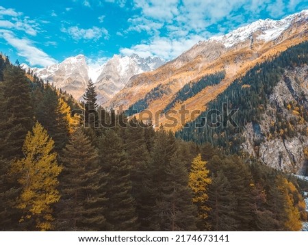 Beautiful view from the drone of the autumn mountains, snow-capped mountains and blue sky with clouds. Landscape photo of a drone with mountains and trees painted in autumn colors