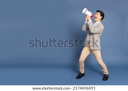 Young Asian business man holding megaphone isolated on blue background, Speaker and announce concept, Full body composition Royalty-Free Stock Photo #2174696091