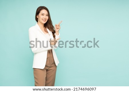 Young beautiful Asian businesswoman smiling and pointing to empty copy space isolated on green background