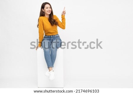 Young Asian woman sitting and pointing to empty copy space isolated on white background, Full body composition Royalty-Free Stock Photo #2174696103