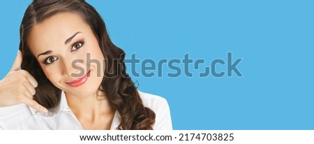 Businesswoman in white confident clothing showing call me hand sign gesture, isolated on bright blue color background. Portrait of smiling gesturing brunette woman at studio. Business concept photo.