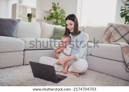 Full body portrait of peaceful girl arms hold cute toddler point finger demonstrate wireless netbook sit floor indoors