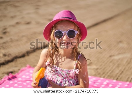 portrait of a little girl wearing a hat and sunglasses with a bottle of sunscreen