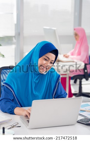 Muslim woman talking on the phone and working on laptop at her workplace