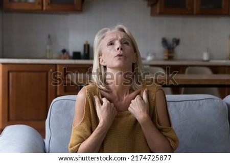 Older woman suffers from high temperature at home feels unwell, looks overheated and unhealthy sit on sofa. Age-related hormonal changes, menopause, need climate control, air-condition system concept Royalty-Free Stock Photo #2174725877