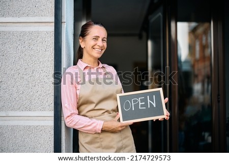 Happy flower shop owner holding sign open while standing at the doorway and looking at camera. Copy space.