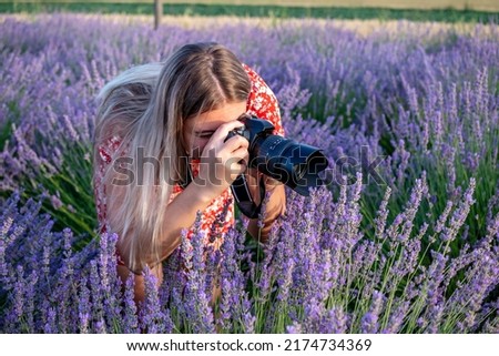 Beautiful woman taking pictures outdoors with a DSLR camera. Female professional photographer, taking photos in a lavender field. 