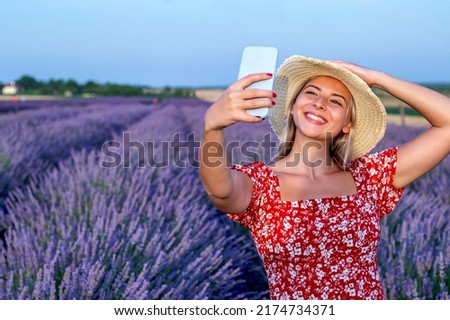 Beautiful blonde woman taking selfie pictures outdoors in a picturesque lavender field. 
