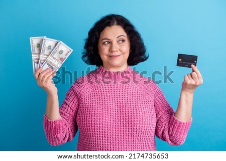 Photo of elderly woman happy positive smile hold cash money dollars credit card isolated over blue color background