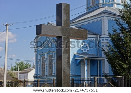 one black big marble cross on the monument at the grave in the cemetery against the background of the blue church and the sky
