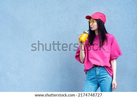Young woman in pink cap and t-shirt drinking orange juice. Blue banner background.
