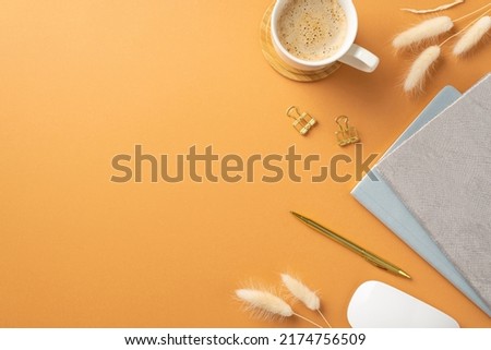 Business concept. Top view photo of workstation cup of coffee on wooden stand white computer mouse planners gold pen binder clips and lagurus flowers on isolated orange background with copyspace