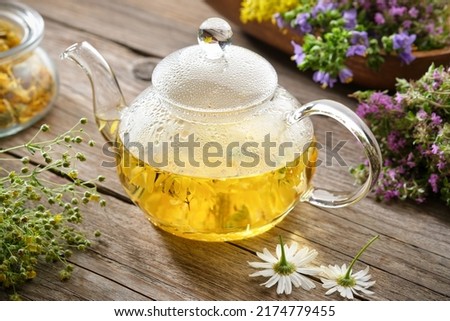 Glass tea kettle of healthy herbal tea, chamomile, calendula, thyme flowers on wooden table. Alternative herbal medicine.  