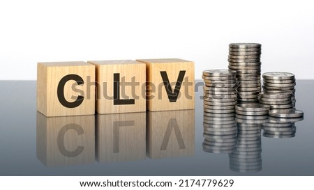 CLV. wooden cubes. blocks lie on a grey background. stacks with coins. reflect from the surface of the table. selective focus. It is an abbreviation for Customer Lifetime Value
