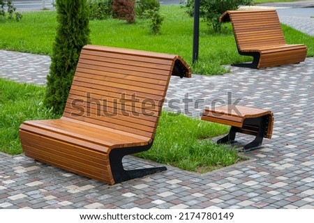 Modern wooden benches standing on the sides of the paved paths of the city park on a rainy day. Royalty-Free Stock Photo #2174780149