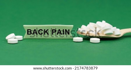 Medicine concept. On a green surface, a wooden spoon with pills and a sign with the inscription - BACK PAIN