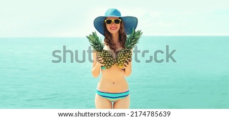 Summer portrait of happy smiling young woman on the beach with funny pineapple wearing straw hat