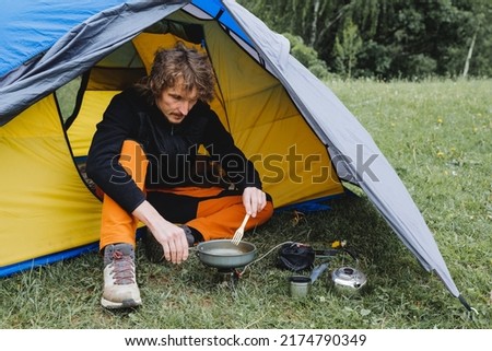 Summer vacation in nature guy sitting in a tent cooking food on a tourist burner, frying eggs in a frying pan, bushcraft hike. High quality photo