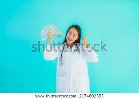 Portrait beautiful young asian doctor woman with a lot of cash and money on blue isolated background