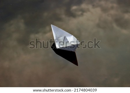 A paper boat floats on water with a reflected sky