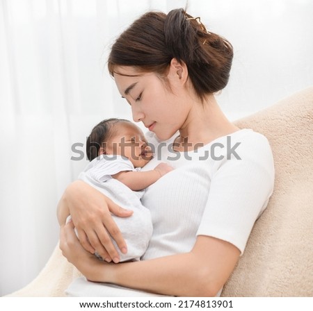 Pretty asian woman smile and holding a newborn baby in her arms. Happy family. Asia mother lifting and looking her adorable infant baby on white. love people concept