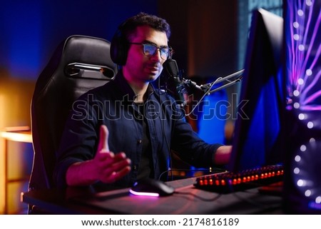 Portrait of streamer playing video games in dark studio with neon accents and speaking to microphone