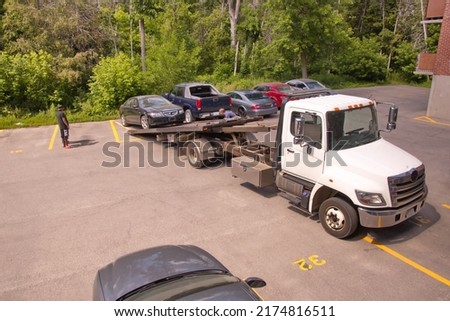 A tow truck driver and a detailed section of the flat bed around him. Royalty-Free Stock Photo #2174816511