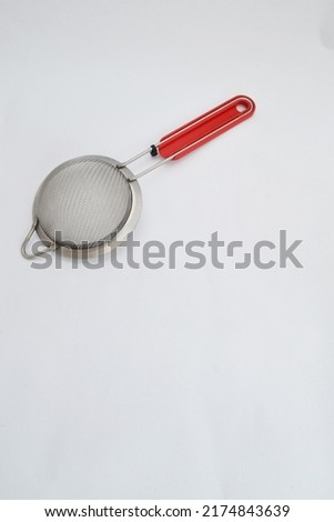 A filter made of silver with a red plastic handle. Copyspace.