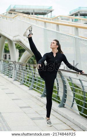 Young dancer girl doing vertical split standing outdoors, she warming up before dance