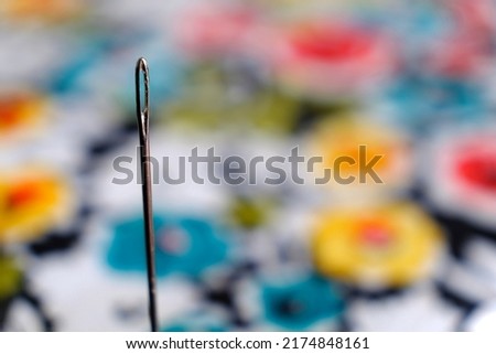A close up photo of a sewing needle pinned against colourful fabric (landscape orientation)