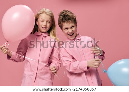happy children boy and girl of school age smile cheerfully while standing on a pink background, the girl holds a pink balloon in her hand. Childhood, friendship, relationships