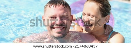 Cheerful couple posing for picture in swimming pool in luxury resort