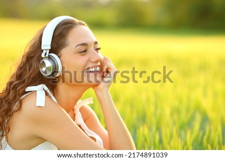 Happy woman listening to music with wireless headphones sitting in a wheat field