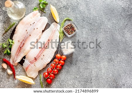 Fresh raw white fish fillet Pangasius with spices and lemon on a stone background with copy space for your text