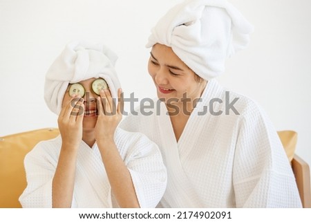 A little girl and beautiful mother wearing spa dress playing and teasing together with pieces of cucumber as a treatment object. The idea for healthcare and love and the relationship of the family.