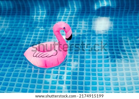 Pink inflatable flamingo in pool water for summer beach background. Minimal summer concept