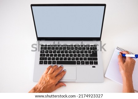 Caucasian female hands browsing on laptop while hand writing on notebook. Blank screen, copy space