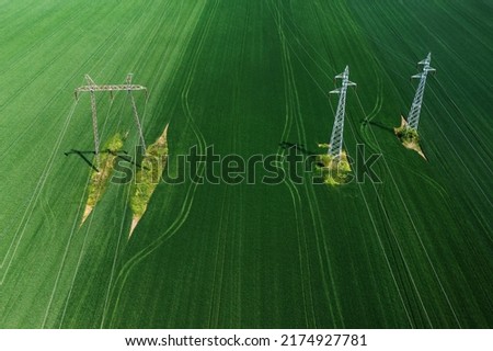 Aerial shot of electricity pylons and transmission towers in cultivated agricultural field from drone pov