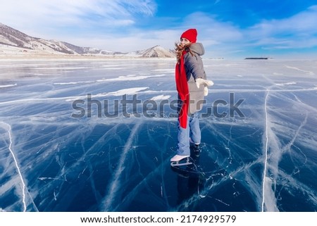 Cheerful woman tourist skates in red hat and scarf on frozen ice of Lake Baikal, sunny winter day.