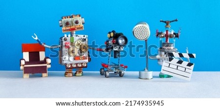 Robotic filmmaking backstage concept. Two robots shoots motion picture television episode or movie. Funny filmmakers director cameraman, cyborg assistant clapperboard on blue background.