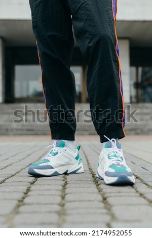 Close photo of athletic man's legs in pants and sneakers on architecture background. Street style.