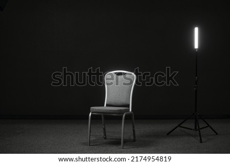 A chair and a light source on the stage for recording an interview or blog. Place for an interview. A chair in a black room Royalty-Free Stock Photo #2174954819